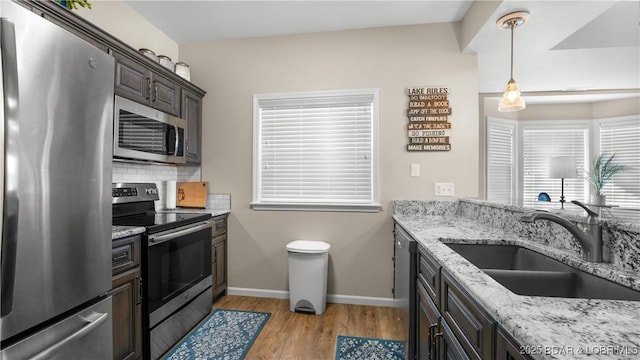 kitchen with light stone counters, stainless steel appliances, a sink, light wood-style floors, and tasteful backsplash