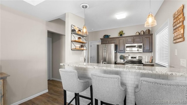 kitchen with decorative backsplash, dark wood-type flooring, decorative light fixtures, a peninsula, and stainless steel appliances