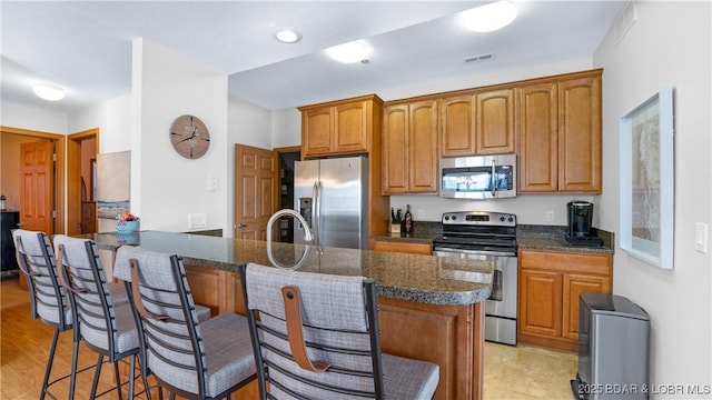 kitchen with visible vents, brown cabinetry, a breakfast bar area, a peninsula, and stainless steel appliances