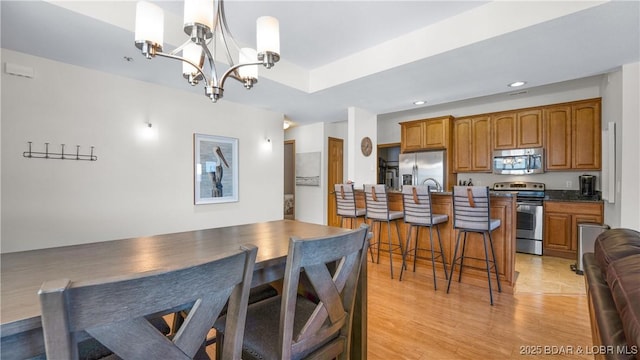 kitchen with stainless steel appliances, a kitchen breakfast bar, light wood-type flooring, brown cabinetry, and an inviting chandelier