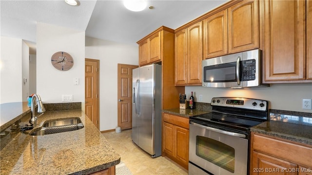 kitchen featuring appliances with stainless steel finishes, dark stone counters, brown cabinets, and a sink