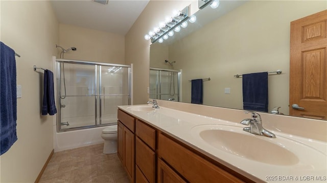 full bathroom featuring double vanity, bath / shower combo with glass door, a sink, and toilet