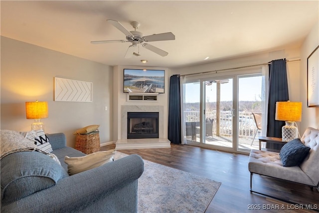 living area with a ceiling fan, a fireplace with raised hearth, and wood finished floors