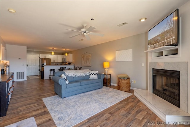 living room featuring dark wood-type flooring, a high end fireplace, visible vents, and baseboards