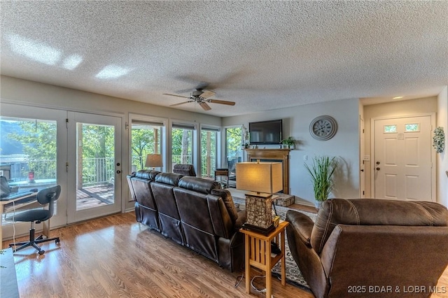 living area with ceiling fan, a fireplace with raised hearth, a textured ceiling, and wood finished floors