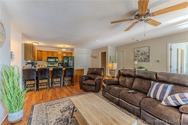 living room with a textured ceiling, light wood finished floors, and a ceiling fan