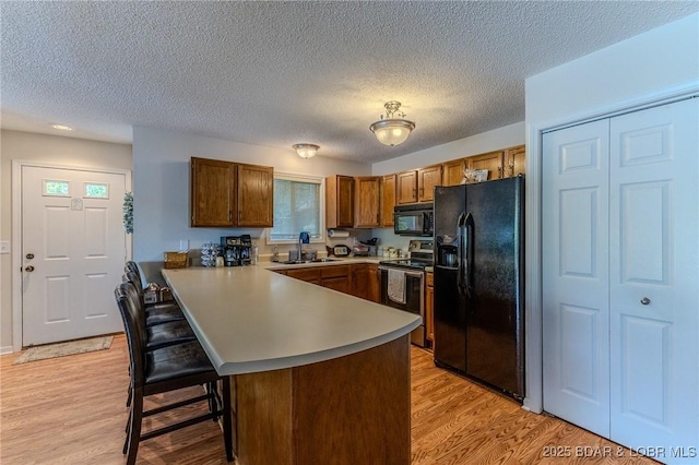 kitchen featuring light wood finished floors, a breakfast bar, a peninsula, black appliances, and a sink