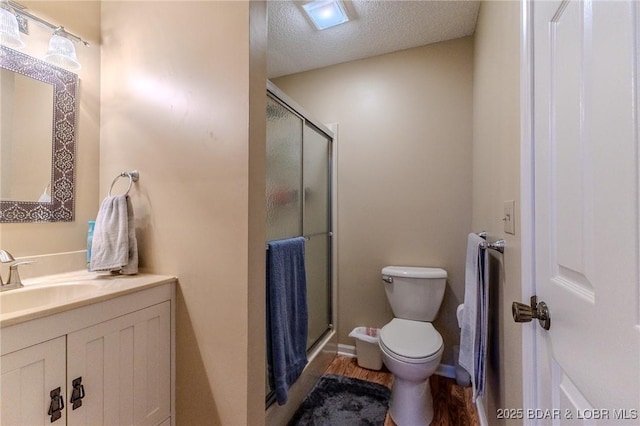 bathroom with toilet, wood finished floors, a textured ceiling, vanity, and a shower stall