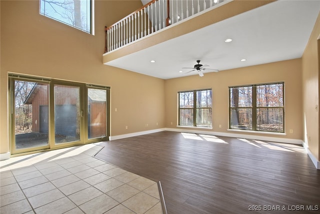 unfurnished living room with recessed lighting, a high ceiling, baseboards, and wood finished floors