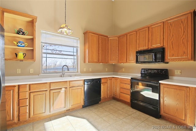 kitchen with a towering ceiling, decorative light fixtures, light countertops, black appliances, and a sink