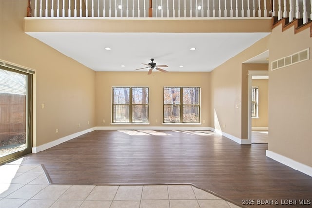 unfurnished living room with ceiling fan, tile patterned flooring, a towering ceiling, visible vents, and baseboards