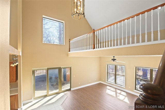 unfurnished living room featuring ceiling fan with notable chandelier, a towering ceiling, baseboards, and wood finished floors