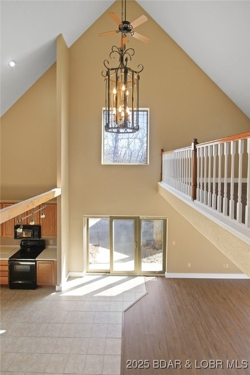 unfurnished living room with high vaulted ceiling, light wood-style floors, and baseboards