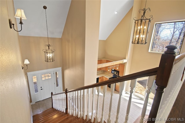 stairs with high vaulted ceiling, a notable chandelier, and wood finished floors