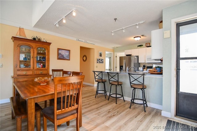 dining area featuring light wood-style floors, baseboards, and a textured ceiling