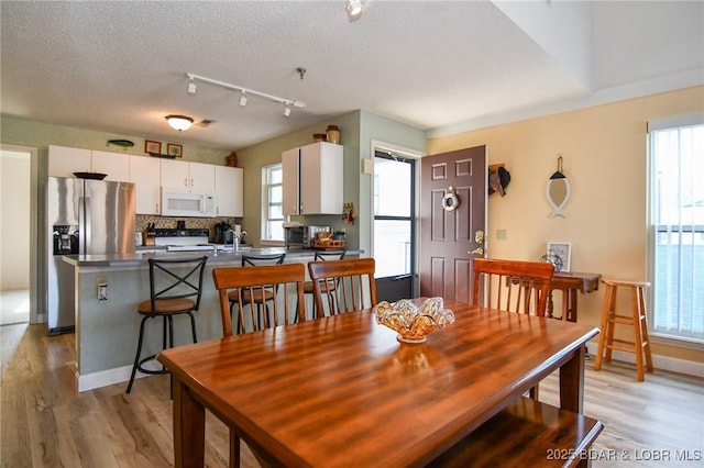 dining area with light wood-style flooring, baseboards, and a textured ceiling