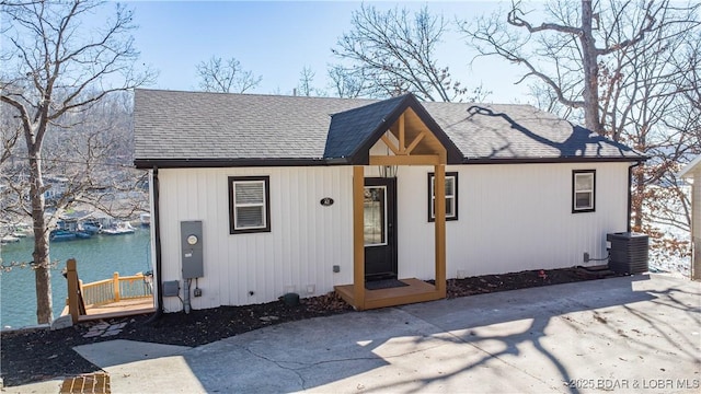 view of front of house featuring roof with shingles, a water view, and central AC unit