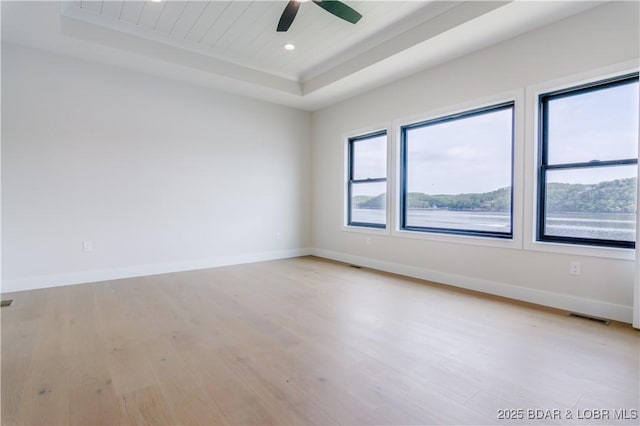 empty room with light wood finished floors, baseboards, and a tray ceiling