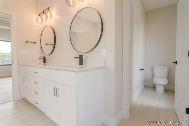 bathroom with double vanity, a sink, toilet, and baseboards