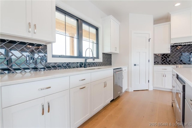 kitchen featuring light wood-style flooring, light countertops, stainless steel dishwasher, white cabinetry, and a sink