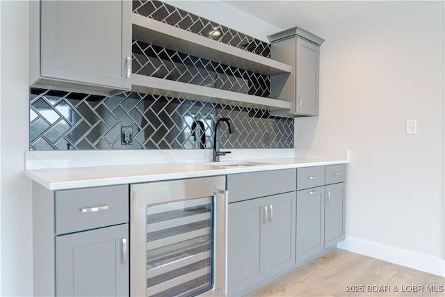 bar with wine cooler, a sink, baseboards, light wood-type flooring, and backsplash