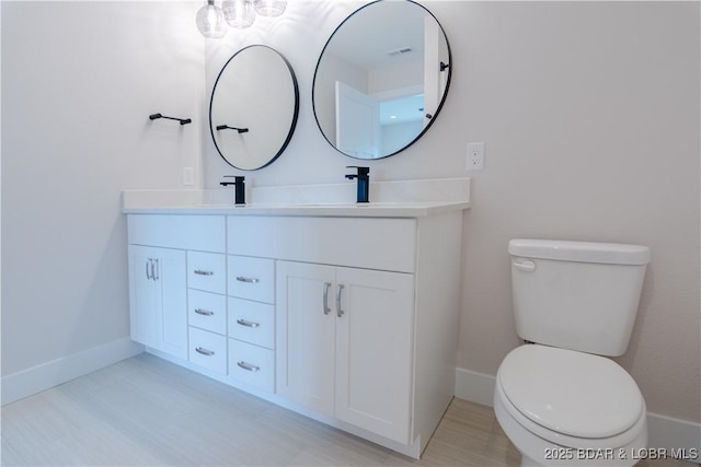 bathroom featuring double vanity, a sink, toilet, and baseboards