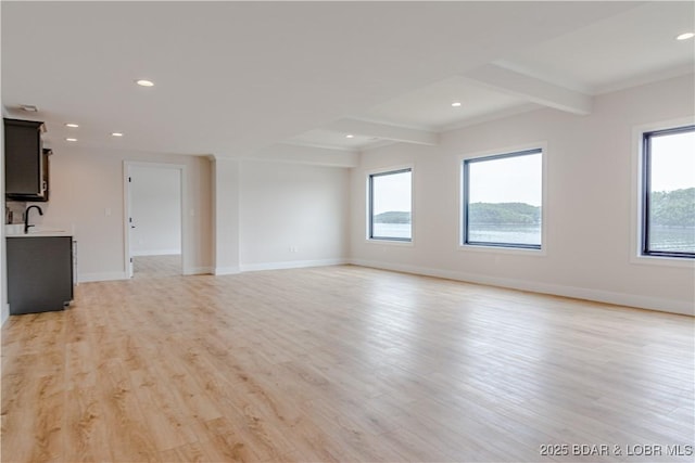 unfurnished living room featuring baseboards, light wood finished floors, beamed ceiling, and a healthy amount of sunlight