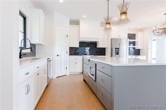 kitchen featuring white cabinets, appliances with stainless steel finishes, light countertops, gray cabinetry, and a sink