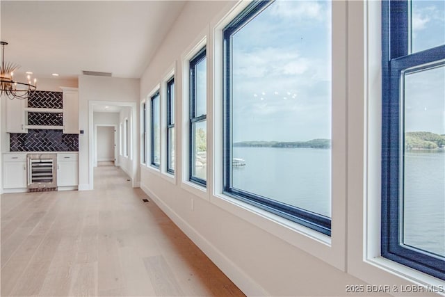 hall featuring beverage cooler, light wood finished floors, a water view, and visible vents