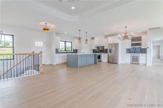 kitchen with light wood finished floors, beverage cooler, a tray ceiling, stainless steel appliances, and white cabinetry