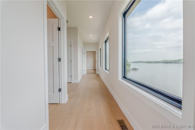 hallway with recessed lighting, a water view, visible vents, baseboards, and light wood finished floors