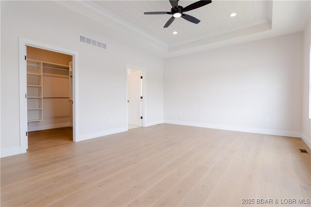 unfurnished bedroom featuring light wood-style flooring, visible vents, a raised ceiling, and baseboards