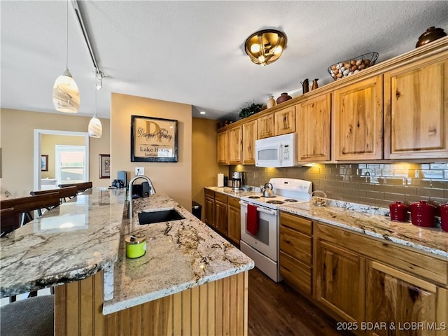 kitchen with light stone counters, a breakfast bar area, white appliances, a sink, and decorative backsplash