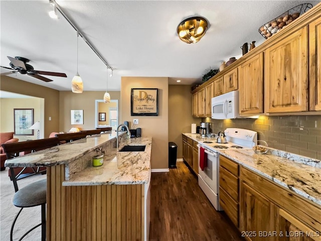 kitchen featuring white appliances, a breakfast bar, a sink, backsplash, and light stone countertops