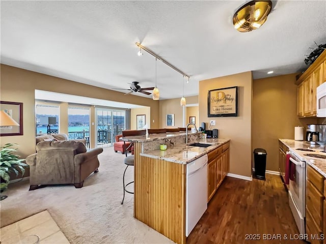 kitchen with white appliances, open floor plan, a peninsula, a kitchen bar, and a sink