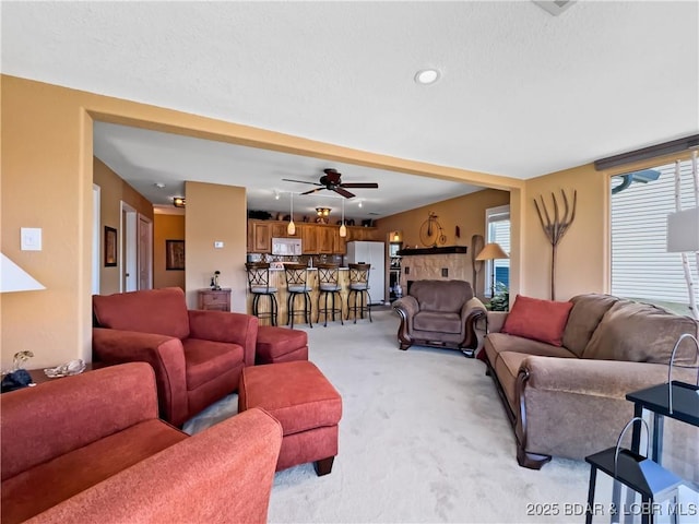 living area featuring light carpet, ceiling fan, and a textured ceiling