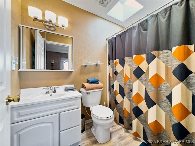 bathroom featuring a skylight, visible vents, toilet, wood finished floors, and vanity