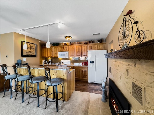 kitchen featuring a breakfast bar, white appliances, visible vents, and brown cabinetry