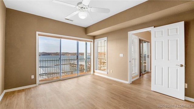 empty room with visible vents, baseboards, a ceiling fan, light wood-style flooring, and a water view