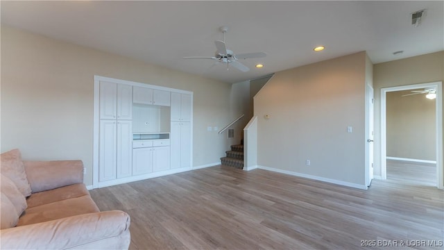 unfurnished living room featuring visible vents, baseboards, ceiling fan, stairway, and light wood-style floors