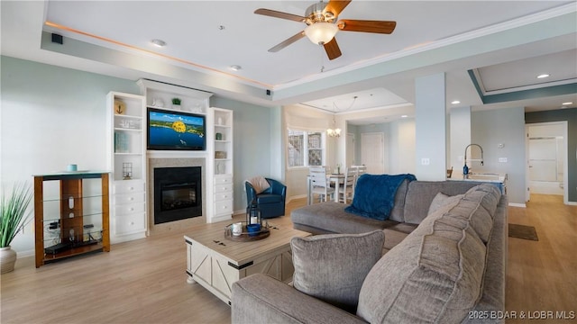 living area featuring light wood finished floors, a raised ceiling, crown molding, and a glass covered fireplace