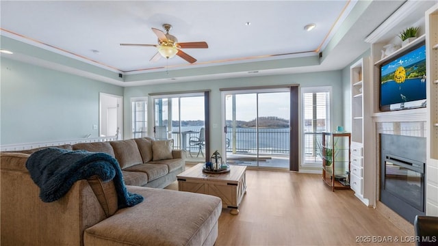 living room with light wood finished floors, a raised ceiling, a wealth of natural light, and a glass covered fireplace