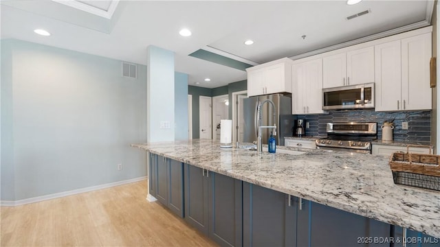 kitchen featuring light wood-style flooring, stainless steel appliances, visible vents, white cabinetry, and decorative backsplash