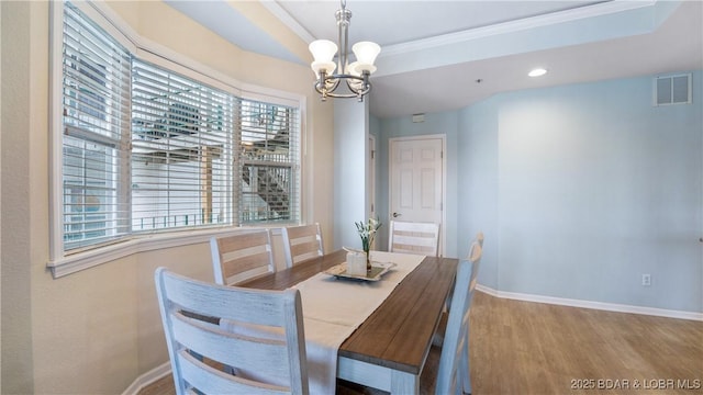 dining area featuring a notable chandelier, wood finished floors, visible vents, baseboards, and a raised ceiling