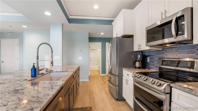 kitchen with crown molding, stainless steel appliances, white cabinetry, a sink, and light wood-type flooring