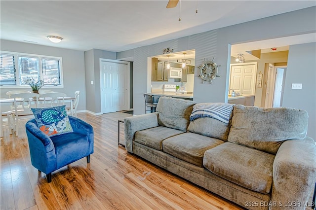 living area with light wood-style floors, ceiling fan, and baseboards