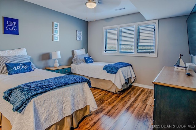 bedroom featuring a ceiling fan, visible vents, baseboards, and wood finished floors