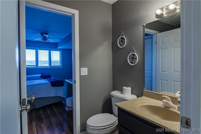 half bath with toilet, ensuite bathroom, ceiling fan, vanity, and wood finished floors