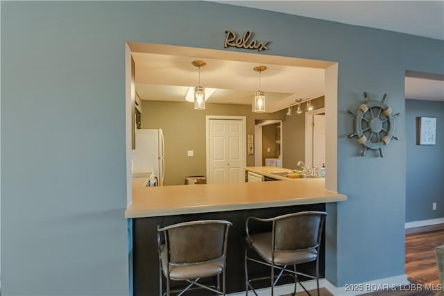 kitchen featuring baseboards, freestanding refrigerator, light countertops, pendant lighting, and a sink