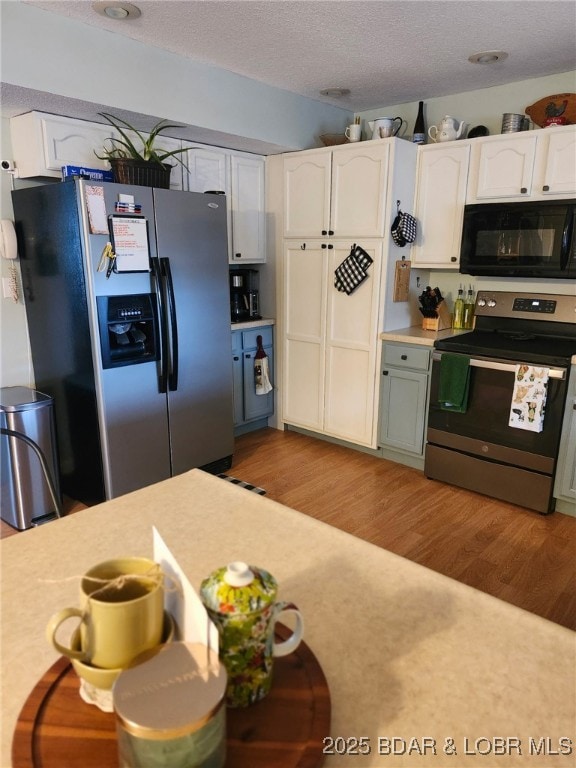 kitchen featuring light countertops, light wood-style flooring, appliances with stainless steel finishes, white cabinets, and a textured ceiling